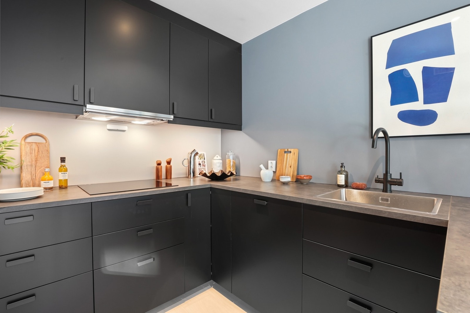 Innredningen har slette, mørke fronter kombinert med laminatbenkeplate med nedfelt stålkum og armatur i sort utførelse. Galleribilde