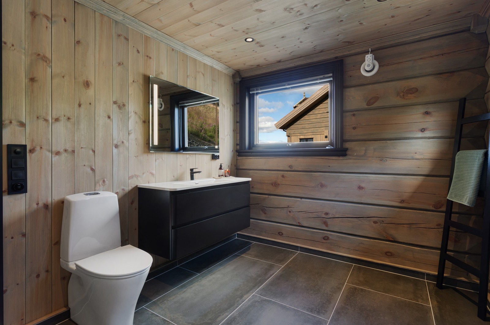 Romslig baderom i hovedetasje med panel/laftet tømmer på vegg og flis på gulv Galleribilde