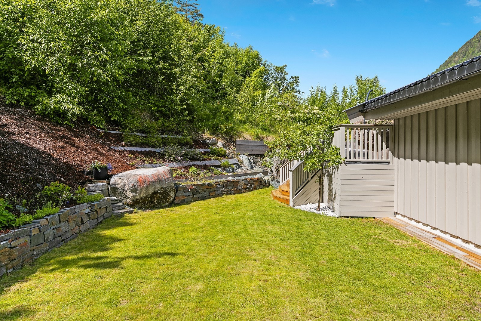 På baksiden av huset er hagen opparbeidet med fine bed og en tilnærmet flat gressplen Galleribilde
