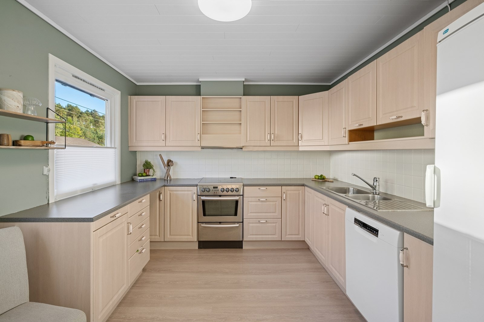 Rommet har en fin og gjennomtenkt fargeplate. Det er montert en tidløs kjøkkeninnredning med lyse og profiterte fronter. Det er rikelig med arbeidssoner og oppbevaringsplass da det er montert godt med skuffeseksjoner, skap og godt med benkeareal. Galleribilde