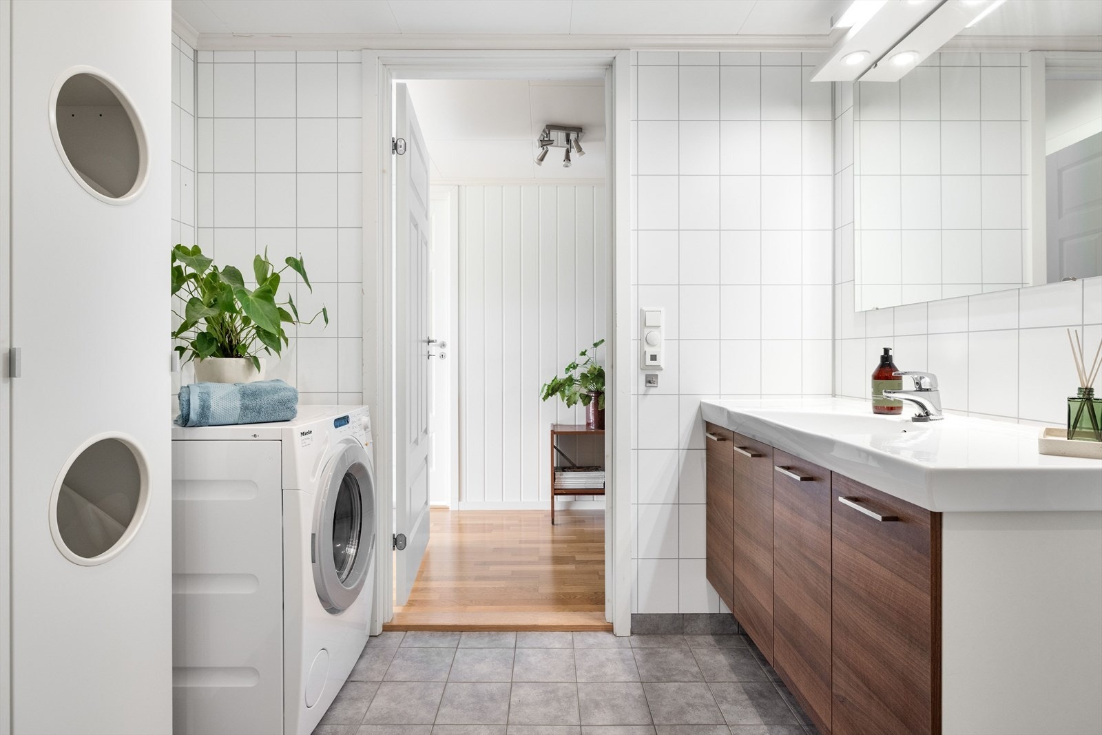 Pen baderomsinnredning med glatte fronter og heldekkende servant, stort speil med belysning over. I hjørnet er det plass og opplegg for vaskemaskin, samt tørketrommel over om ønskelig. Galleribilde