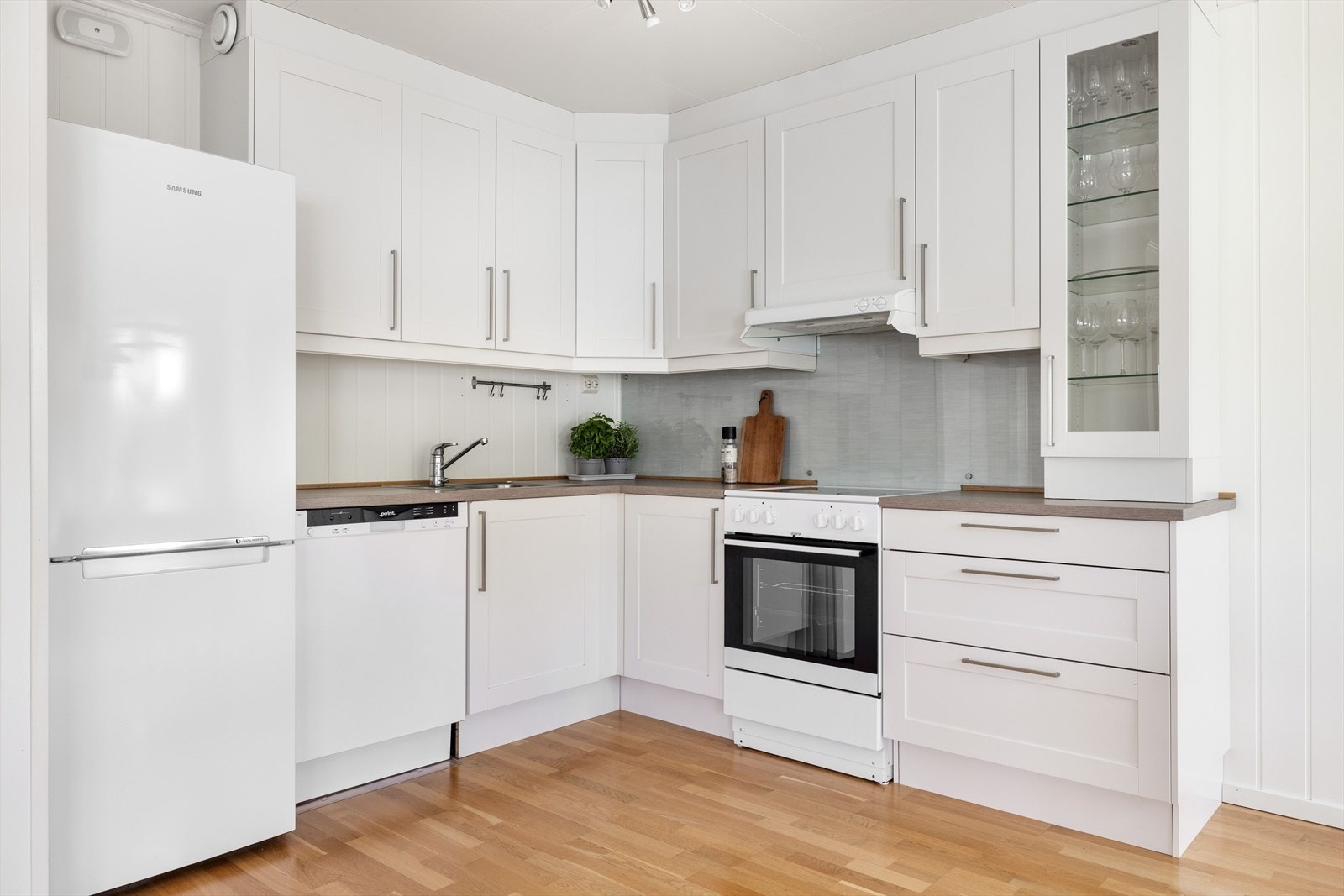 Innredningen har lyse profilerte fronter og laminert benkeplate med nedfelt oppvaskkum. Praktisk med glassplate i benkeryggen ved platetoppen og belysning under de takhøye overskapene. Det er mekanisk avtrekk tilkoblet balansert ventilasjon. Galleribilde