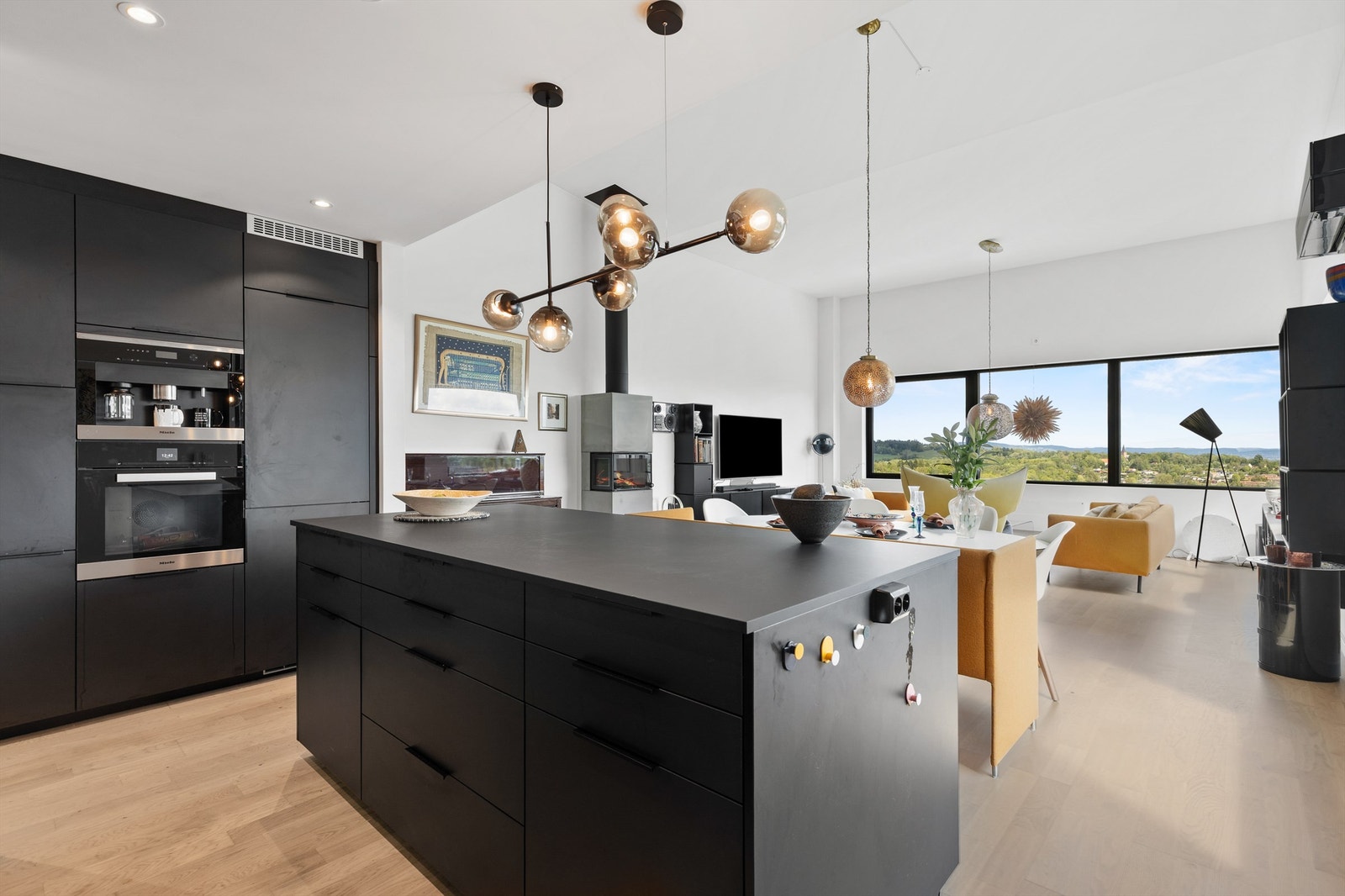 Pent kjøkken med spiseplass, åpent inn mot en lys stue med god takhøyde og flott utsikt. Galleribilde