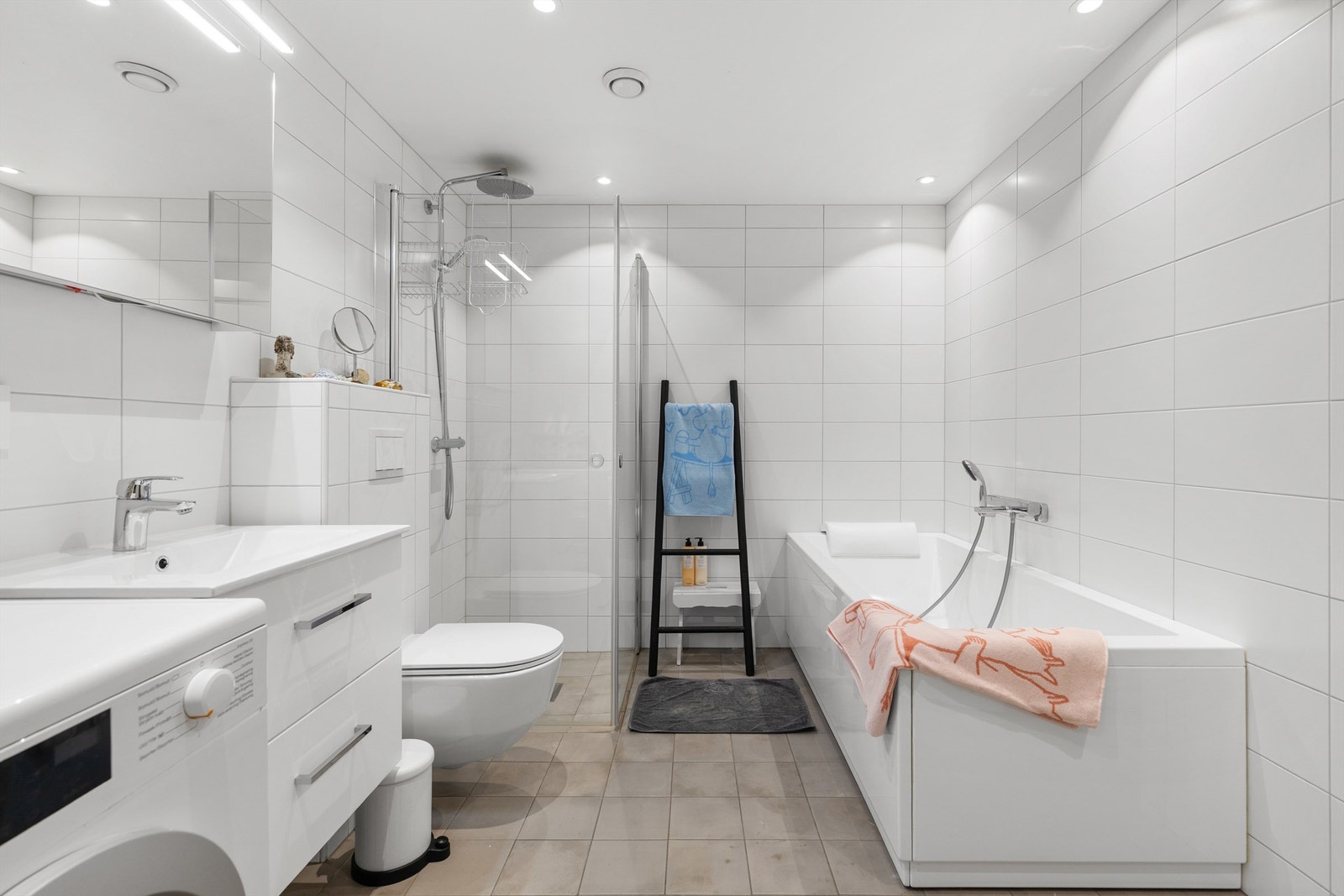 Bad 2 i 1.etasje ligger ved trimrommet. Fliser på vegger og gulv. Slett malt tak. Enkelservant med ett-greps armatur. Servantinnredning. Speilskap. Dusj med svingbare dusjdører. Vegghengt toalett. Badekar. Avtrekk tilkoblet balansert ventilasjonsanlegg. Galleribilde