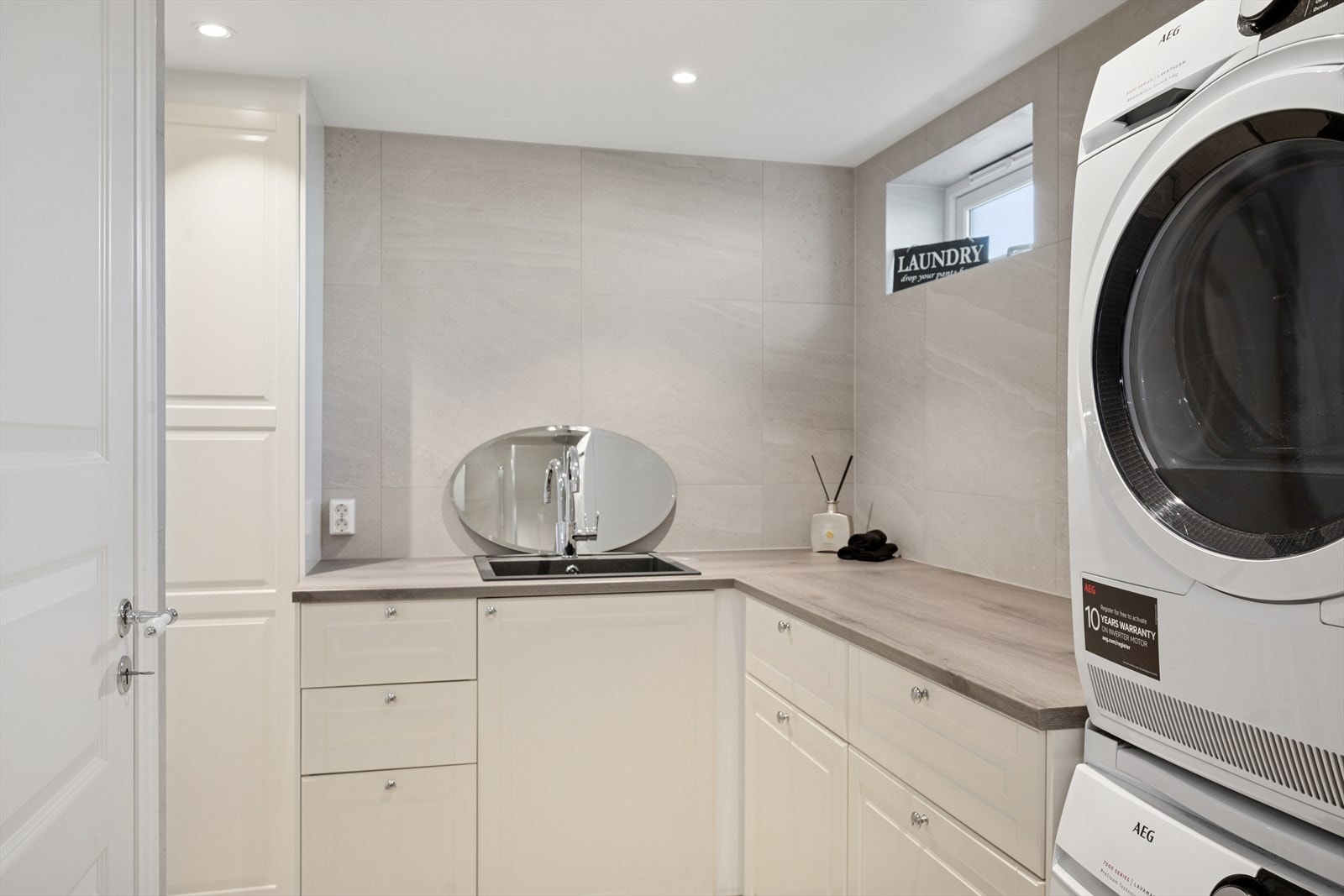 Rommet er utstyrt med toalett, dusjhjørne med glassdører, servant med skuffer, innredning og benkplate med utslagsvask i kompositt, samt opplegg for vaskemaskin. Galleribilde