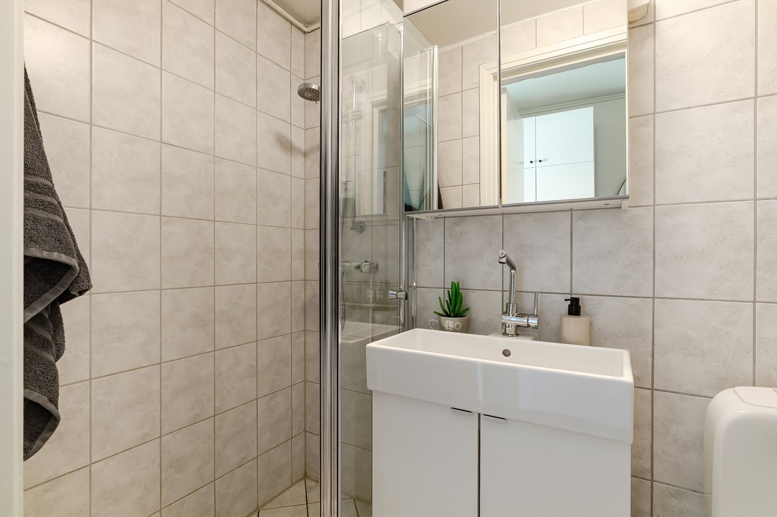 Badet ligger med inngang fra entréen og er på 2,3 kvm. Det har flislagt gulv med varmekabler, flislagte vegger og malt slett himling. Det inneholder dusjvegger i glass, gulvmontert toalett og servant med innredning. Galleribilde