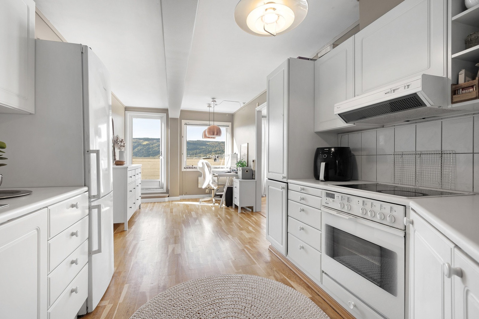 Innredningen er lys med profilerte fronter, flislagt mellom benk og overskap, og integrerte hvitevarer som komfyr, platetopp og oppvaskmaskin. Galleribilde