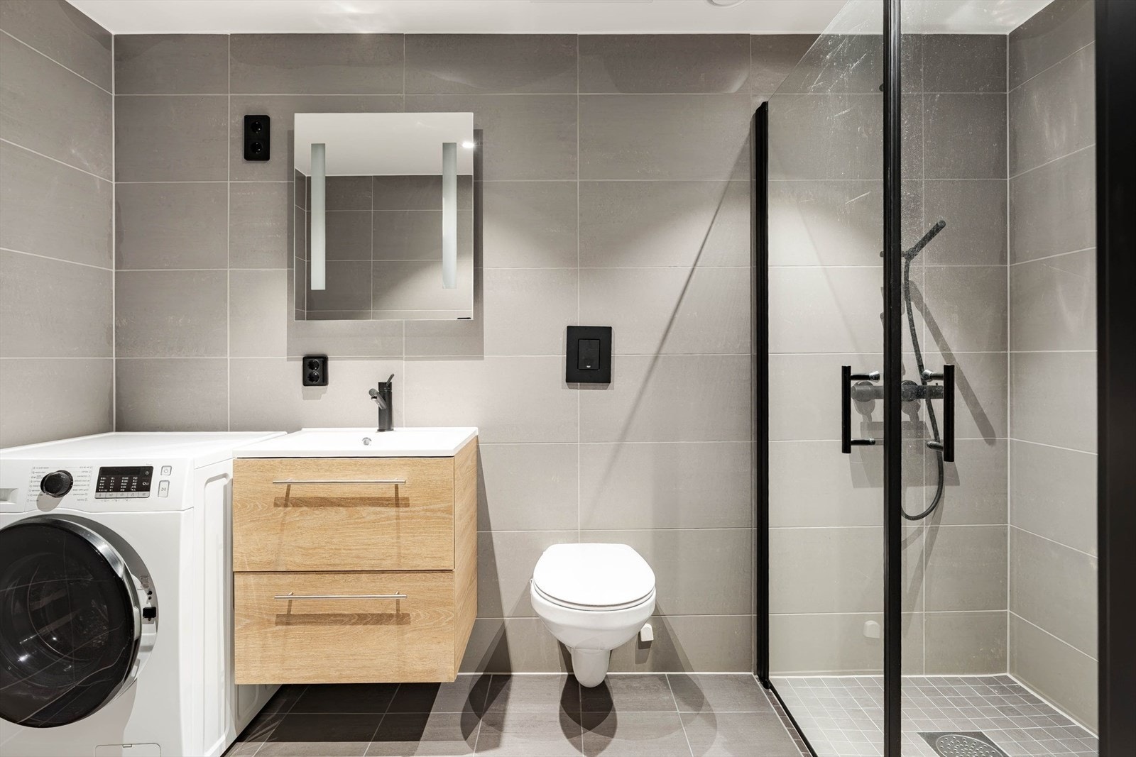 Delikat, flislagt bad med dusj og opplegg for vaskemaskin Galleribilde