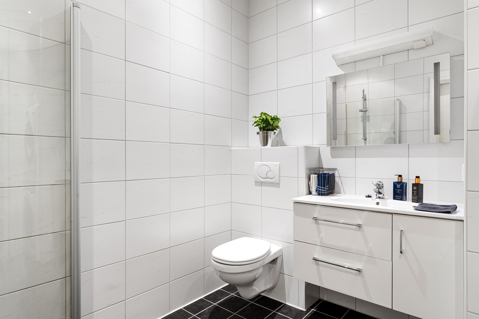 Helfliset bad på ca. 5,70 m² med varmekabler. Innredet med innfellbart dusjhjørne av glass, vegghengt klosett, møblement med servant, dobbel stikkontakt, speil med integrert lys og lysarmatur med stikkontakt. Galleribilde