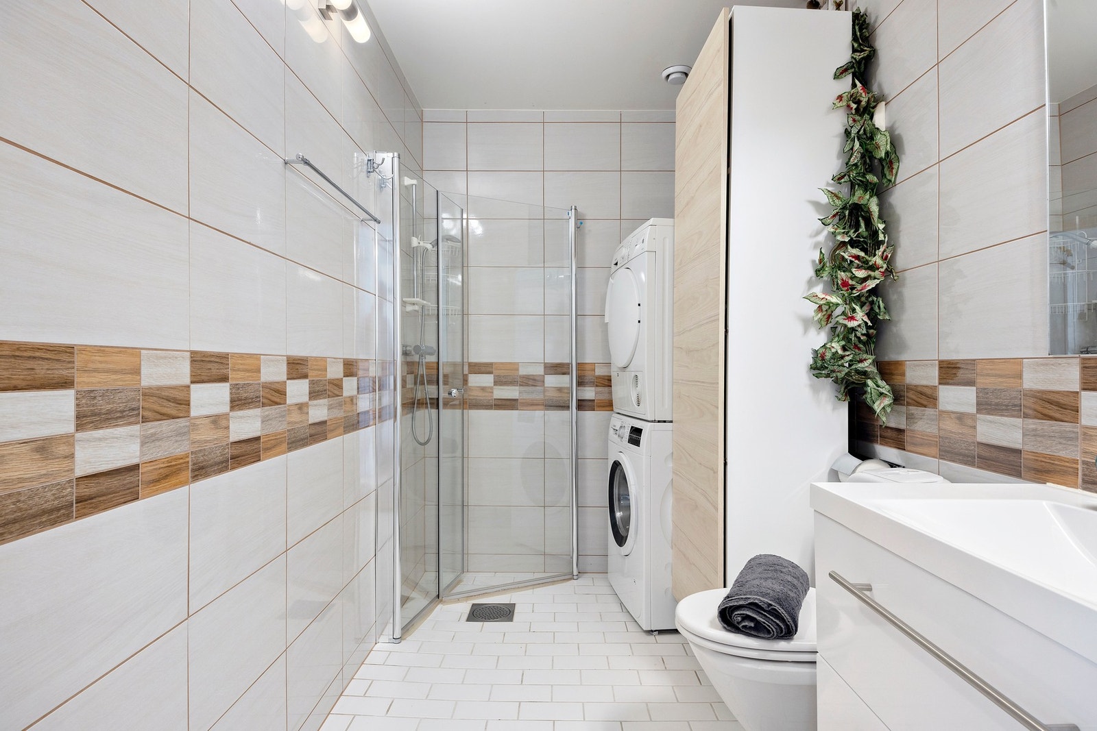 Dusjsonen er smart plassert i hjørnet med glassvegger, og badet er utstyrt med gulvstående toalett samt opplegg for vaskemaskin og tørketrommel. Galleribilde