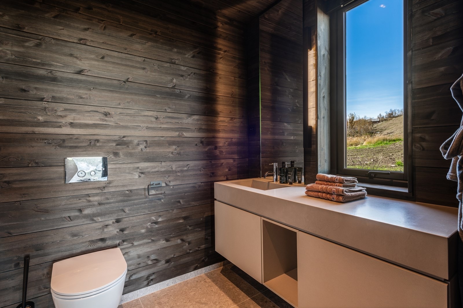 Badet har fliset gulv med elektriske varmekabler, veggene har fliser og panel/tømmer. Galleribilde