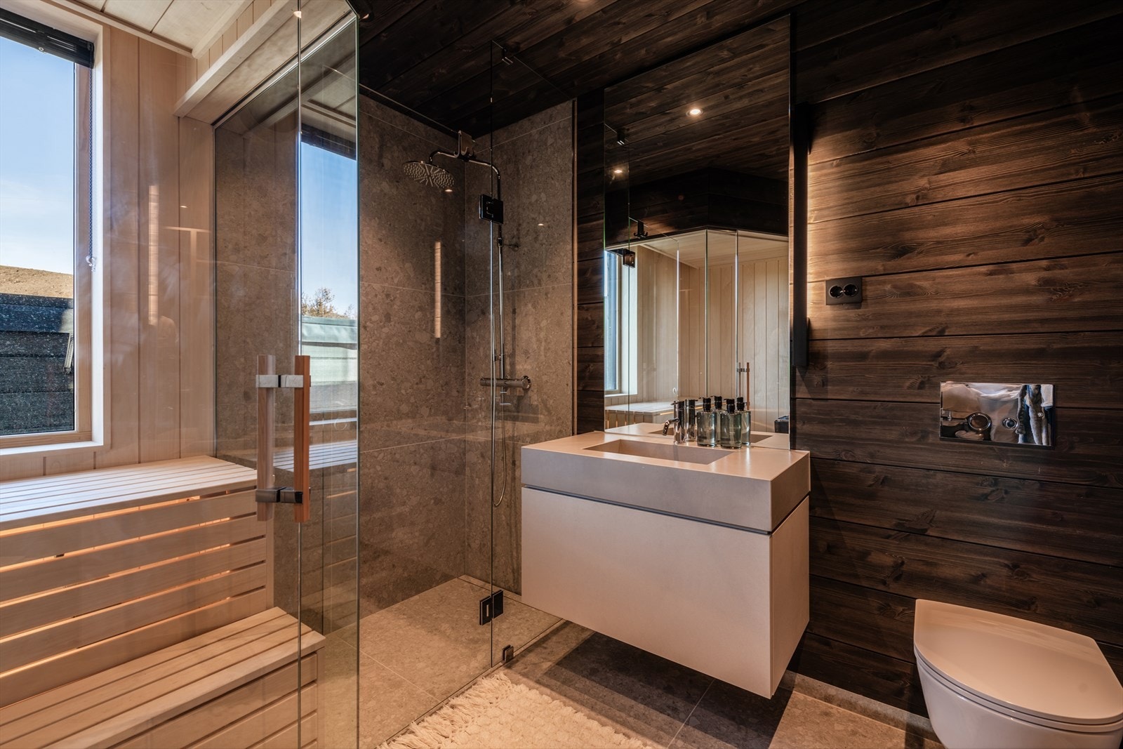 Badet er innredet med dusjone med glassdør og regnfall-dusjhode, vegghengt toalett, servant med underskap og speil. Galleribilde