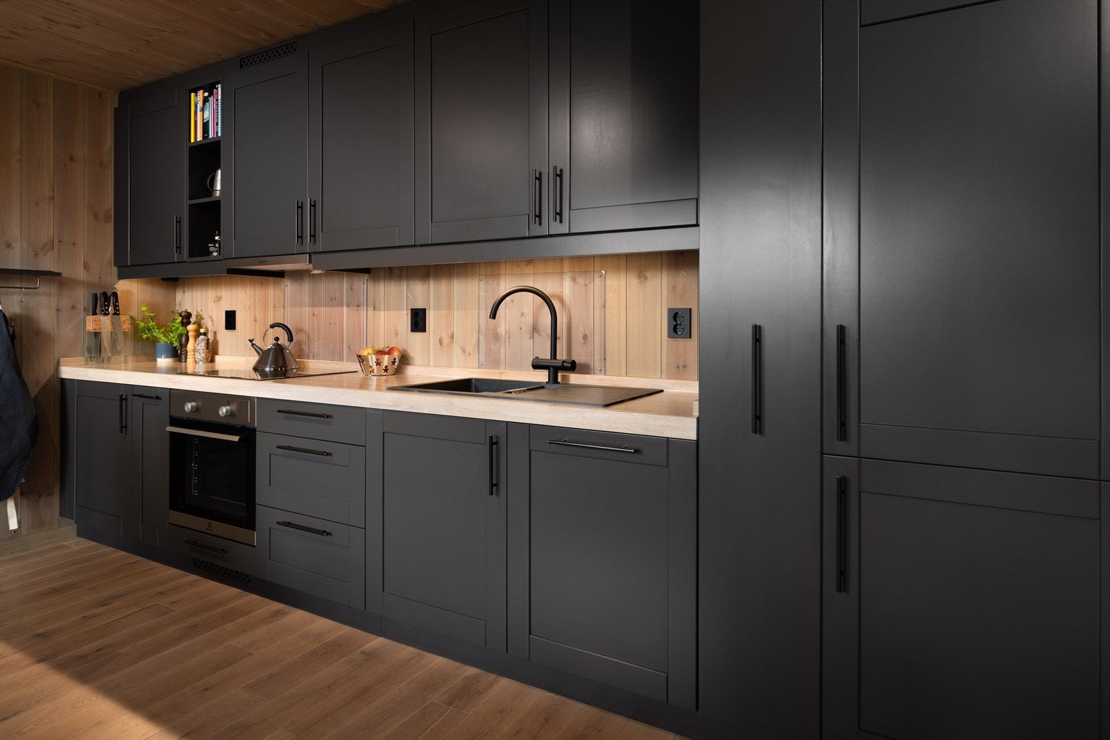 Innredning med profilerte behandlet fronter, solid heltre benkeplate og integrerte hvitevarer. Splashguard på vegg ved platetopp og vask. Galleribilde