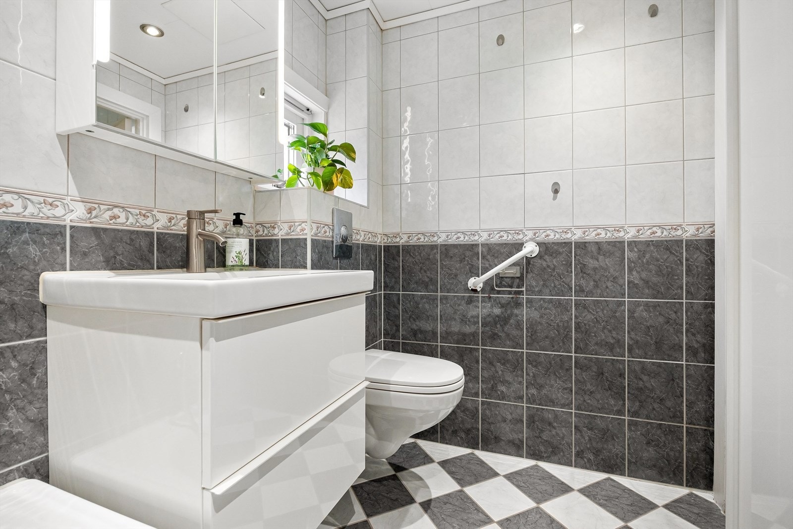 Badet er innredet med benkeskap med servant, badekar, vegghengt toalett og varmekabler i gulv. Galleribilde