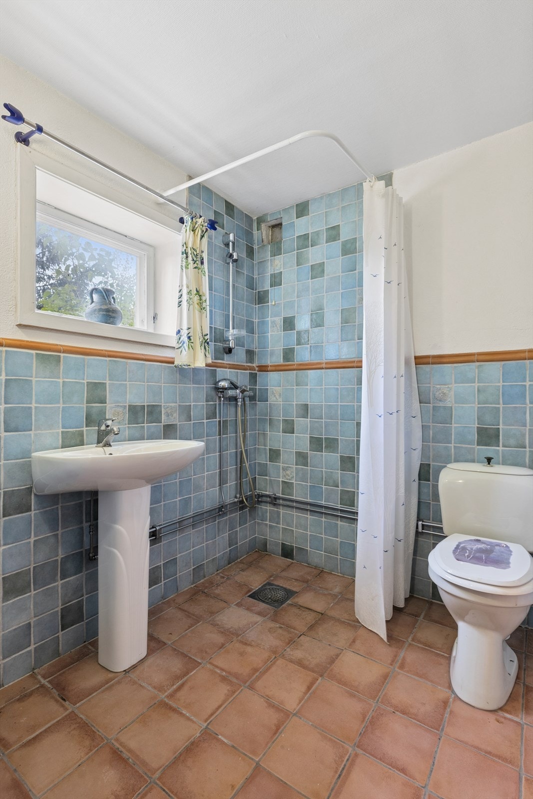 Eldre bad med fliser på gulvet og tapet på vegg. Badet er utstyrt med servant på underskap, speil, belysning og dusj. Ikke godkjent innredet. Det er også badstue. Galleribilde