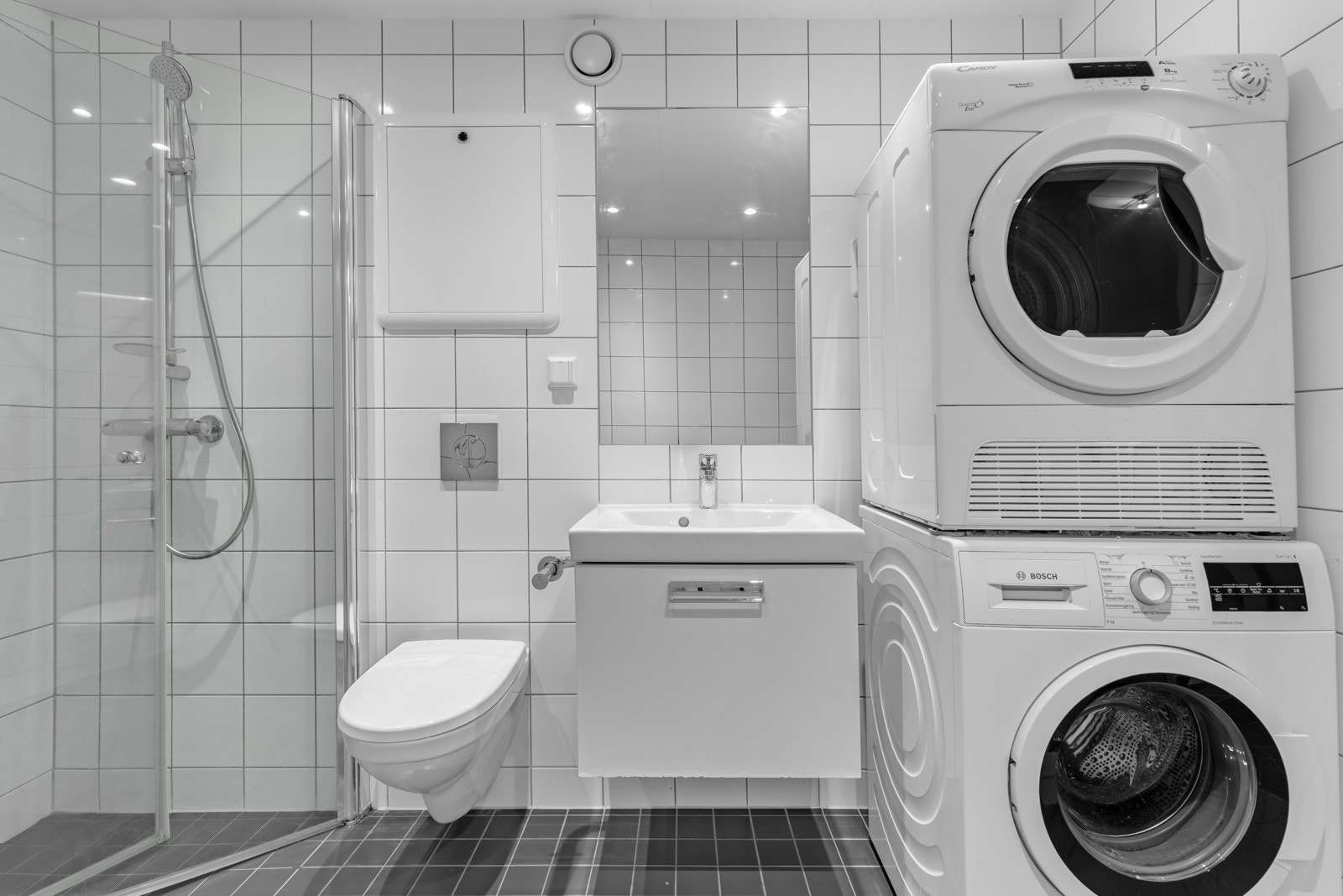 Baderommet inneholder servant med underskap, speil, vegghengt toalett og dusjhjørne med innfellbare glassdører. Galleribilde