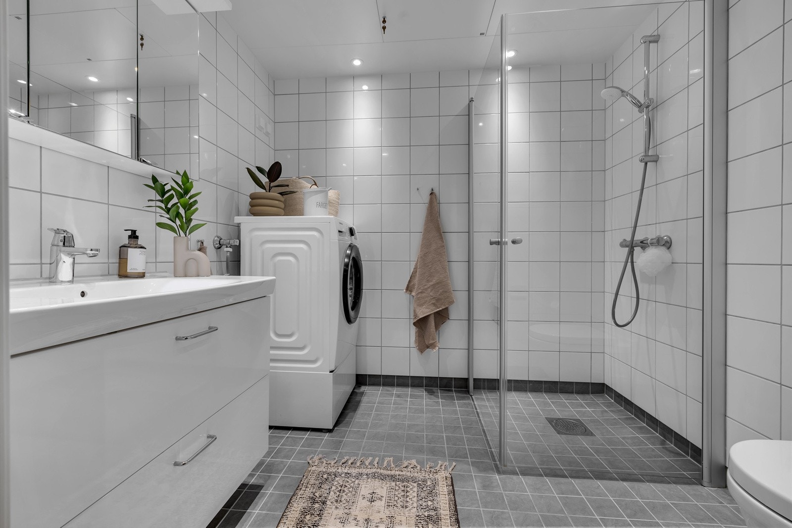 Pent bad som er flislagt på gulv og vegger. Innfelt belysning i tak, innfellbare glassdører i dusjsonen og opplegg for vaskemaskin og tørketrommel Galleribilde