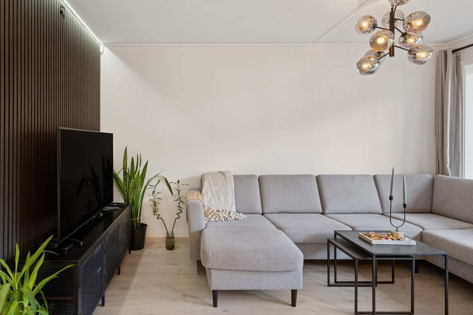 Lys og innbydende stue med moderne uttrykk og god plass til sofagruppe. De lyse flatene og det stilrene spilepanelet skaper en harmonisk og lun atmosfære. Galleribilde