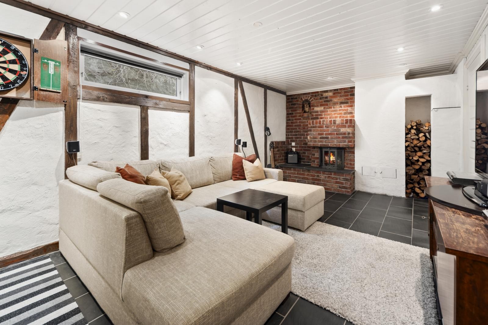 Kjellerstue med god plass til sofagruppe. Hyggelig peis med praktisk og dekorativ vedstabler. Direkte adkomst til garasjen. Galleribilde