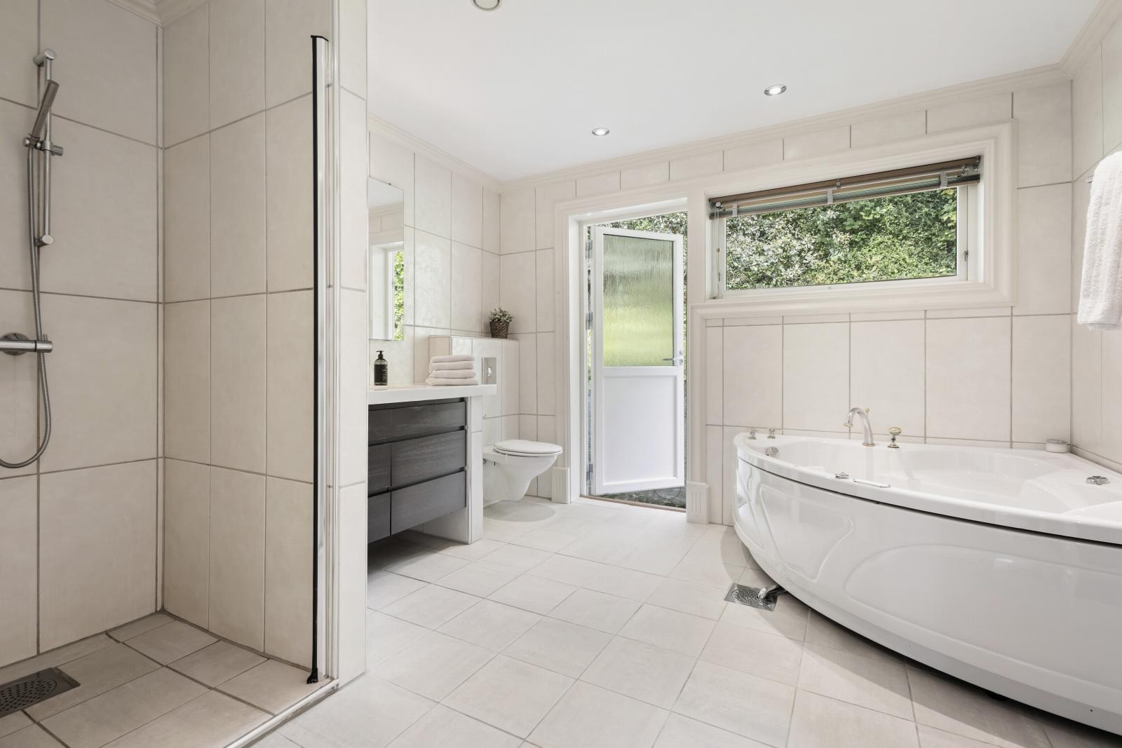 Lyst, flislagt baderom innredet med dusjnisje, hjørnebadekar, vegghengt klosett og servant med møbelsnekret innredning og Corian benkeplate. I tillegg er det sjakt for skittentøy ned til vaskerommet i underetasjen. Galleribilde