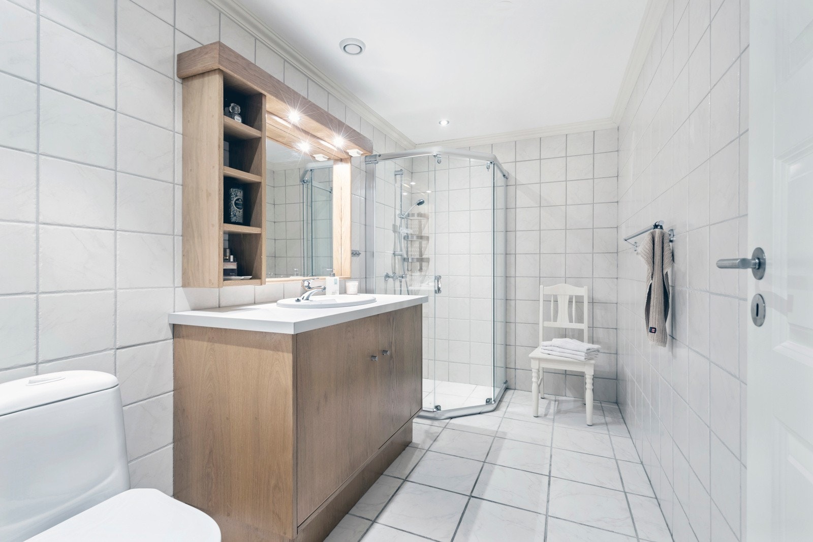 Lyst, flislagt baderom, innredet med dusjnisje, klosett og servant med servantskap i heltre eik fra møbelsnekker. God belysning på badet med downlights i tak samt lys integrert over speil. Galleribilde