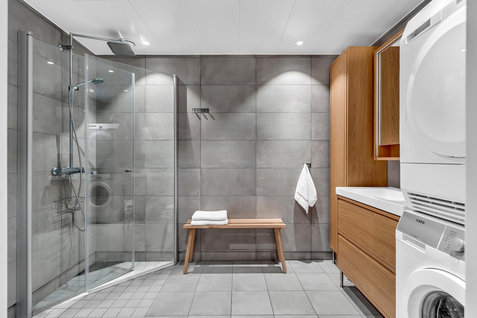 Lekkert flislagt bad med moderne innredning, dusjhjørne med glassdører og praktisk opplegg for vaskemaskin og tørketrommel. Galleribilde