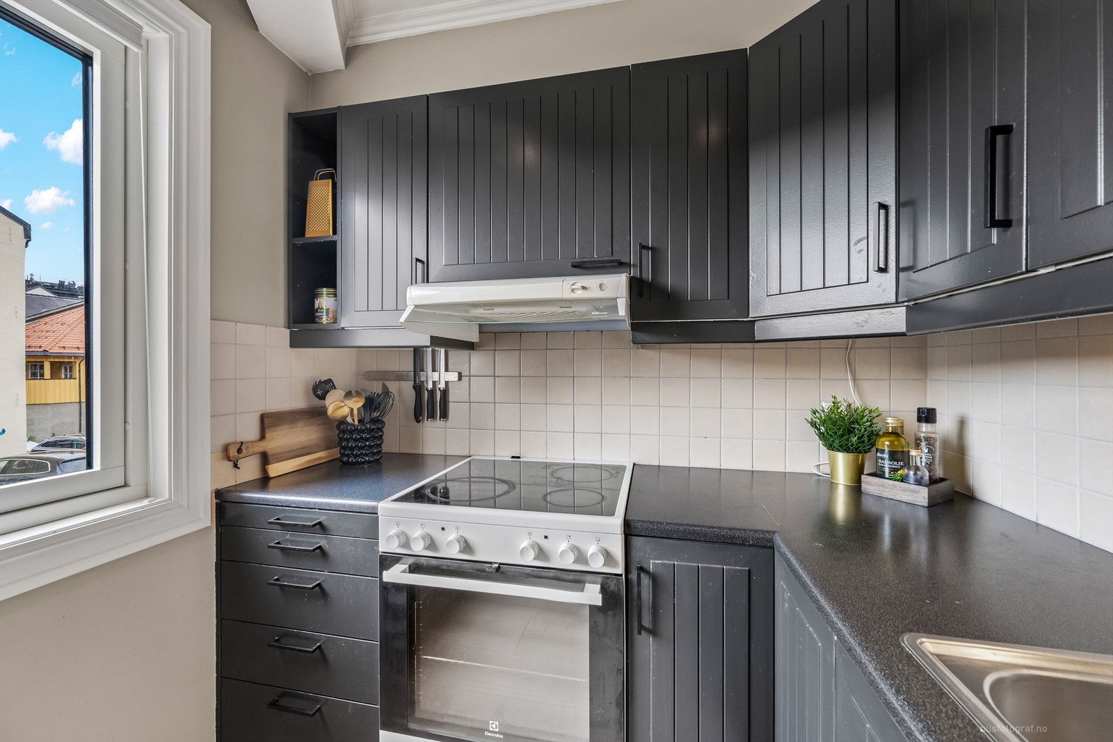 Flislagte felt på vegg over benkeplater av laminat og lysarmaturer under overskap Galleribilde