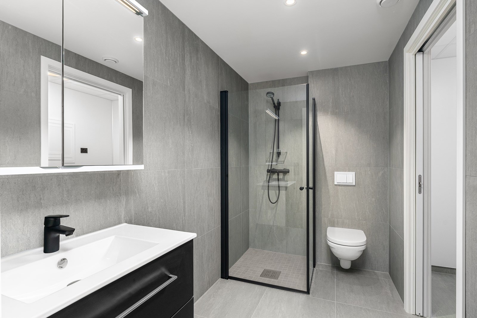 Lekkert bad med fliser på gulv og vegger. Utstyrt med vegghengt toalett, dusj, samt baderomsinnredning med heldekkende servant, speil og god belysning. Galleribilde