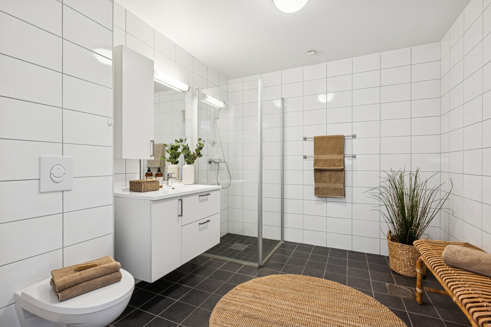 Et moderne og lyst baderom utstyrt med servantinnredning, dusjhjørne, vegghengt toalett og opplegg for vaskemaskin. Galleribilde