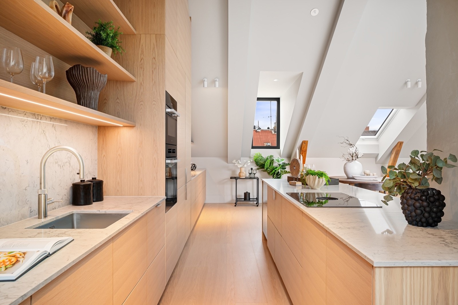 Nordisk preg; glatte fronter i eikestruktur, kombinert med en tynn, lys benkeplate i marmorert komposittstein både på øy, benk og som backsplash. Galleribilde