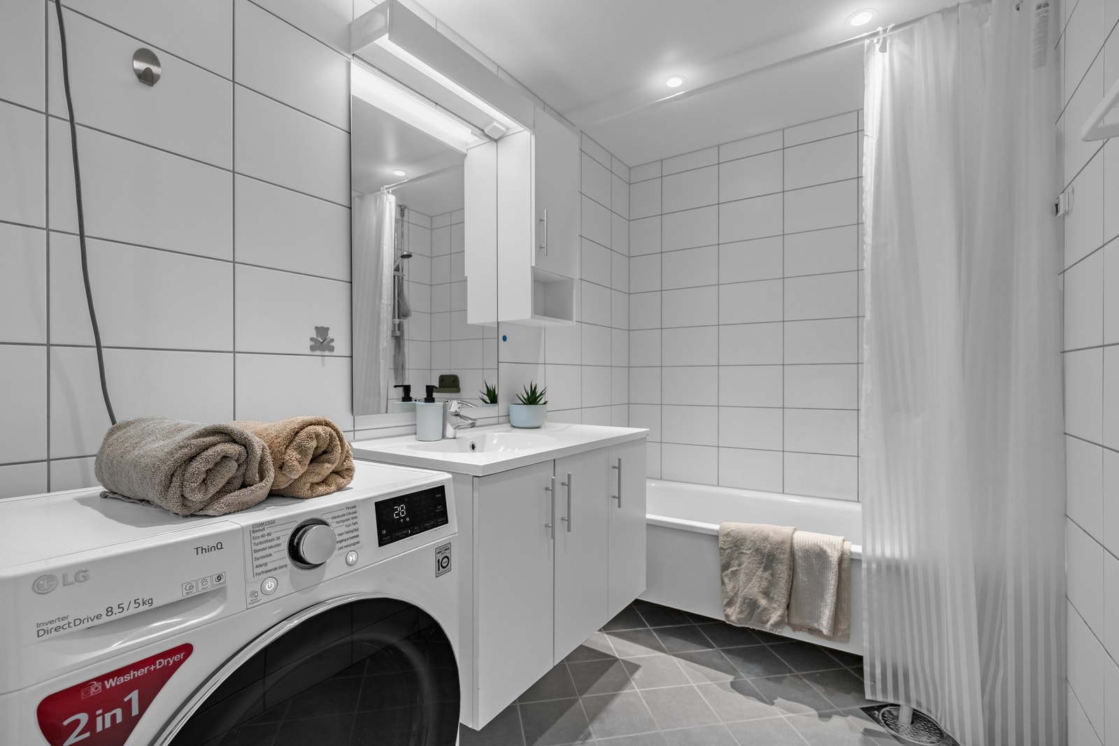 Badet har flislagte vegger og gulv, samt malt tak. Rommet er utstyrt med nedfelt servant, badekar og opplegg for vaskemaskin. Galleribilde
