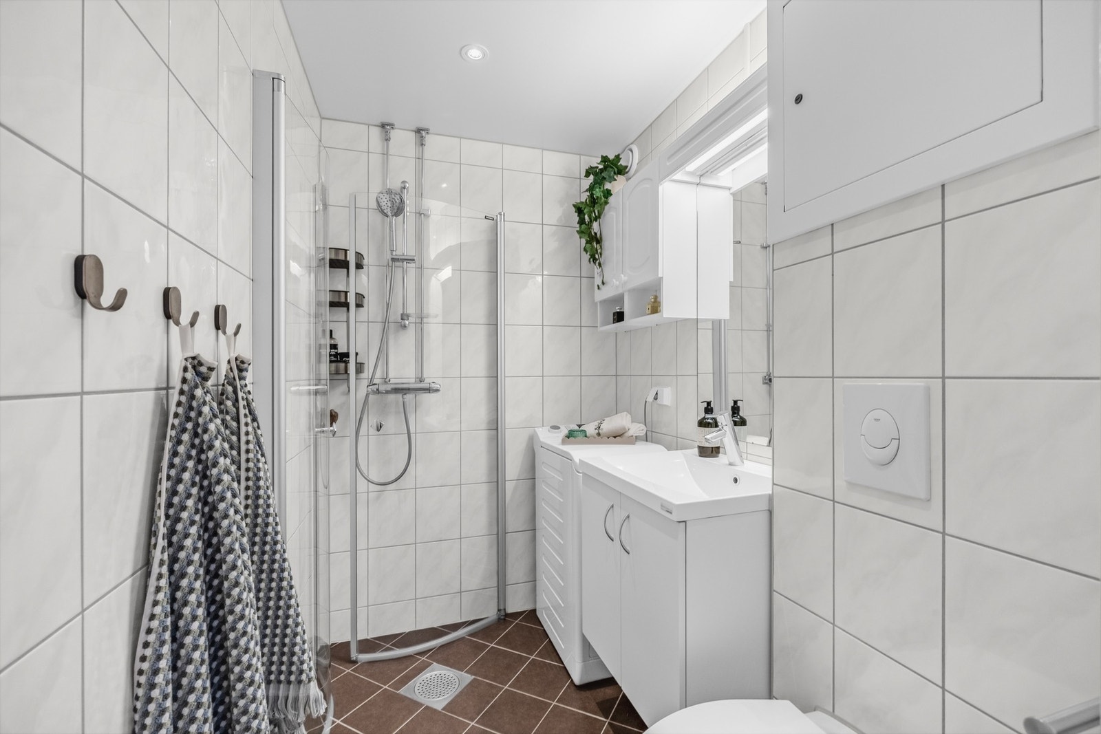 Badet er utstyrt med dusjhjørne med svingdører, termostatstyrt blandebatteri, vegghengt klosett, servantskap med glatte fronter, og heldekkende servant. Speil med lysarmatur over servant. Galleribilde