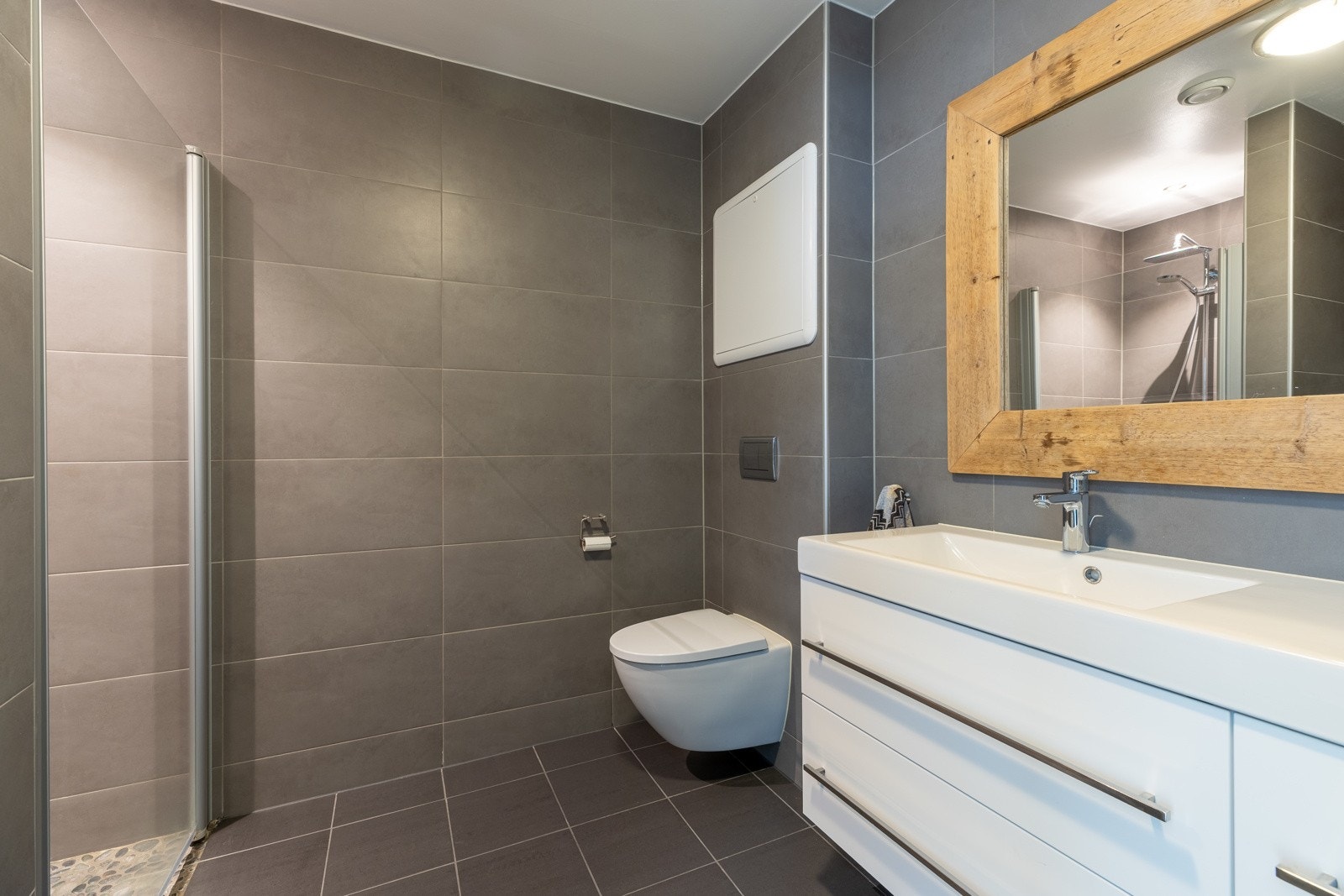 Badet er av god størrelse og er innredet med dusjhjørne, vask med skuffeseksjon og speil, vegghengt wc og opplegg for vaskemaskin. Galleribilde