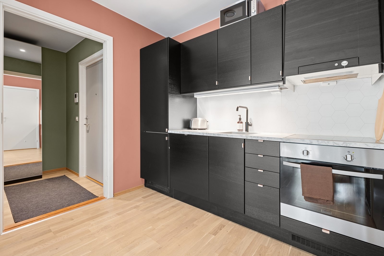 Kjøkken med sorte fronter, lys benkeplate i marmormønster og integrerte hvitevarer. God skap- og benkeplass, samt åpent og praktisk oppsett. Galleribilde