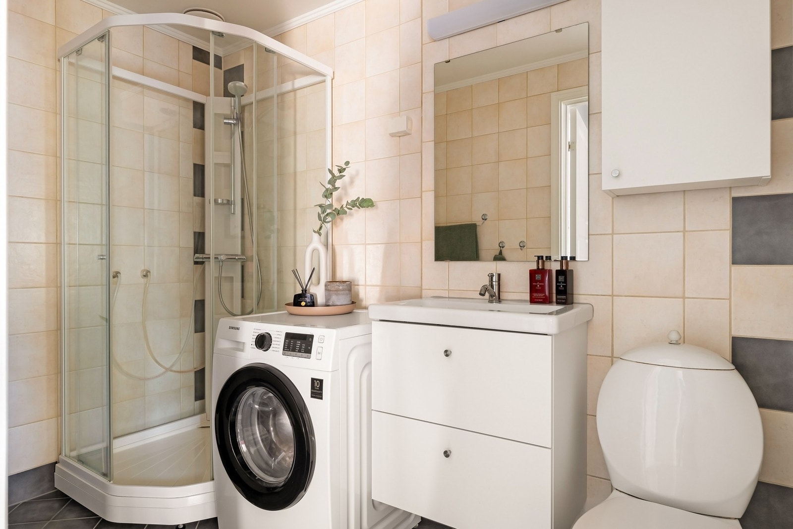 Flislagt bad/vaskerom med dusjkabinett, toalett, servant m/innredning og vegghengt skap, samt opplegg for vaskemaskin. Galleribilde