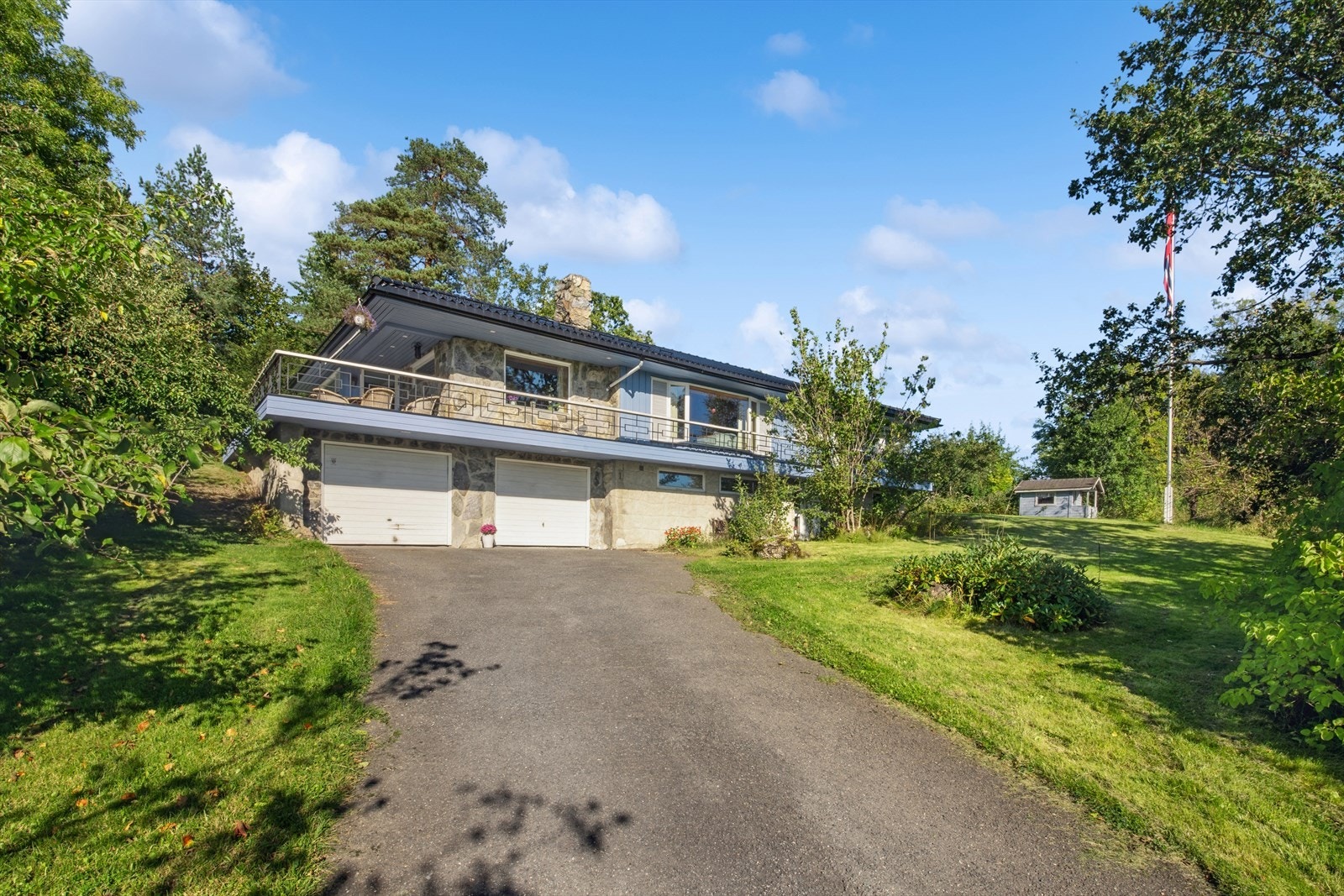Fasade med integrert dobbelgarasje og innkjørsel, omkranset av grøntarealer Galleribilde