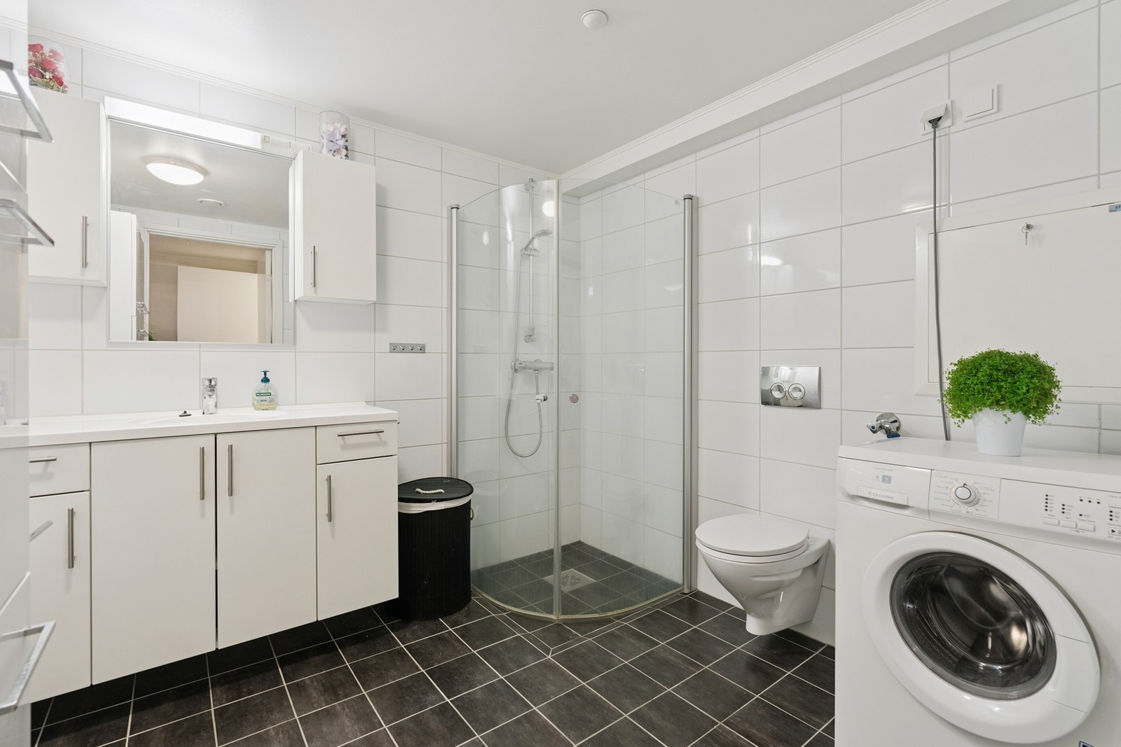 I leiligheten er det et romslig bad med vegghengt servant, toalett og skap, samt opplegg for både vaskemaskin og tørketrommel. Galleribilde