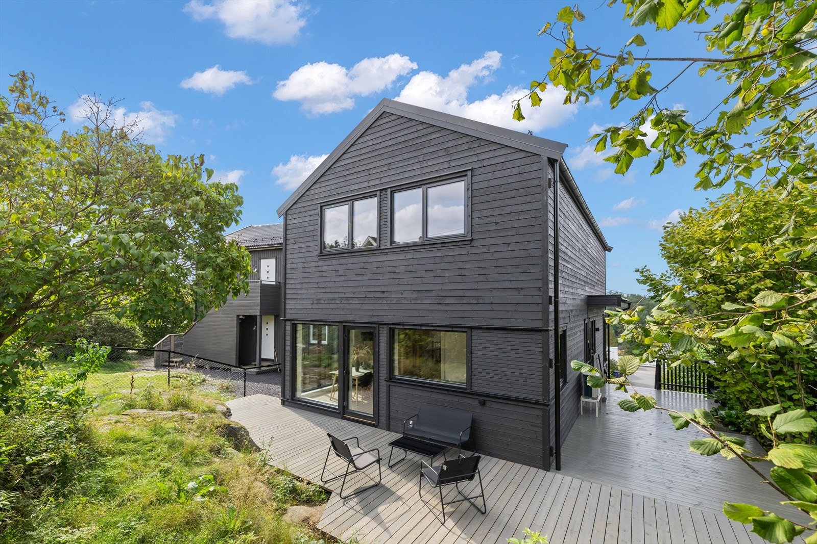 Boligen er omgitt av grønne omgivelser som gir en lun atmosfære og et hjem der inne- og uterom smelter sammen på en naturlig måte. Galleribilde