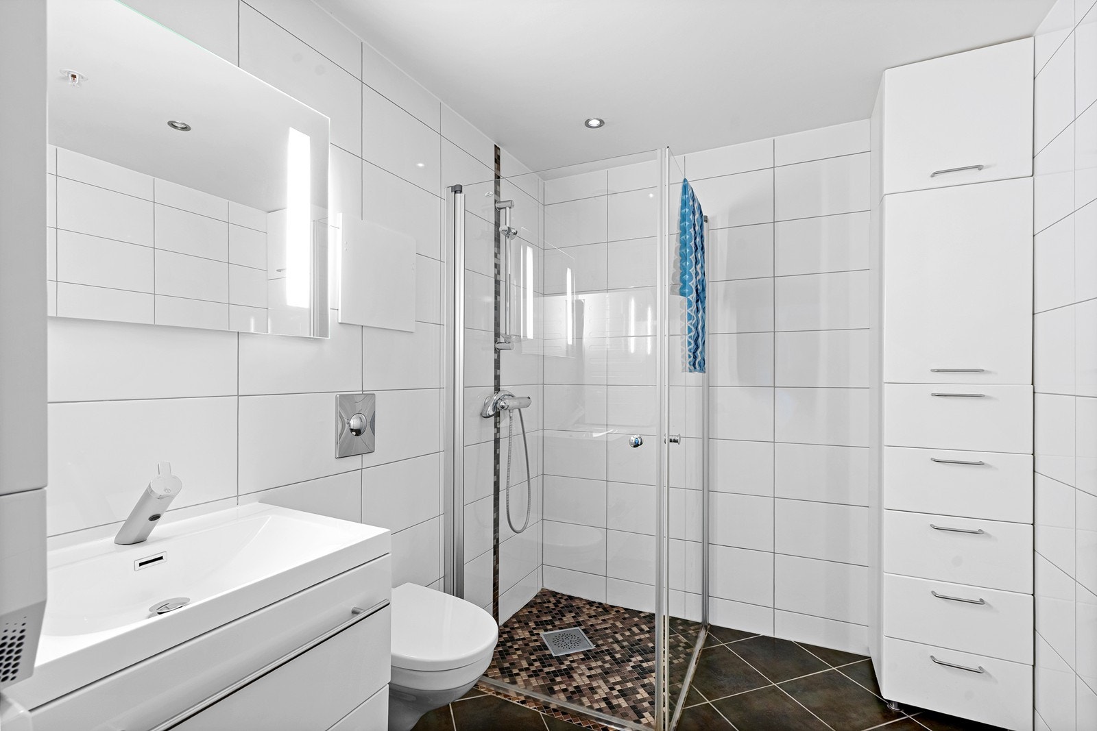 Helfliset baderom med lyse vegger og kontrastfarget gulv. Mosaikkfliser på gulv og stripe på vegg i dusjsone, er en lekker detalj. Galleribilde