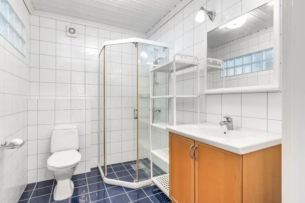 Flislagt baderom med vannbåren gulvvarme. Badet er innredet med servant med innredning og speil, dusjhjørne med glassvegger og toalett Galleribilde