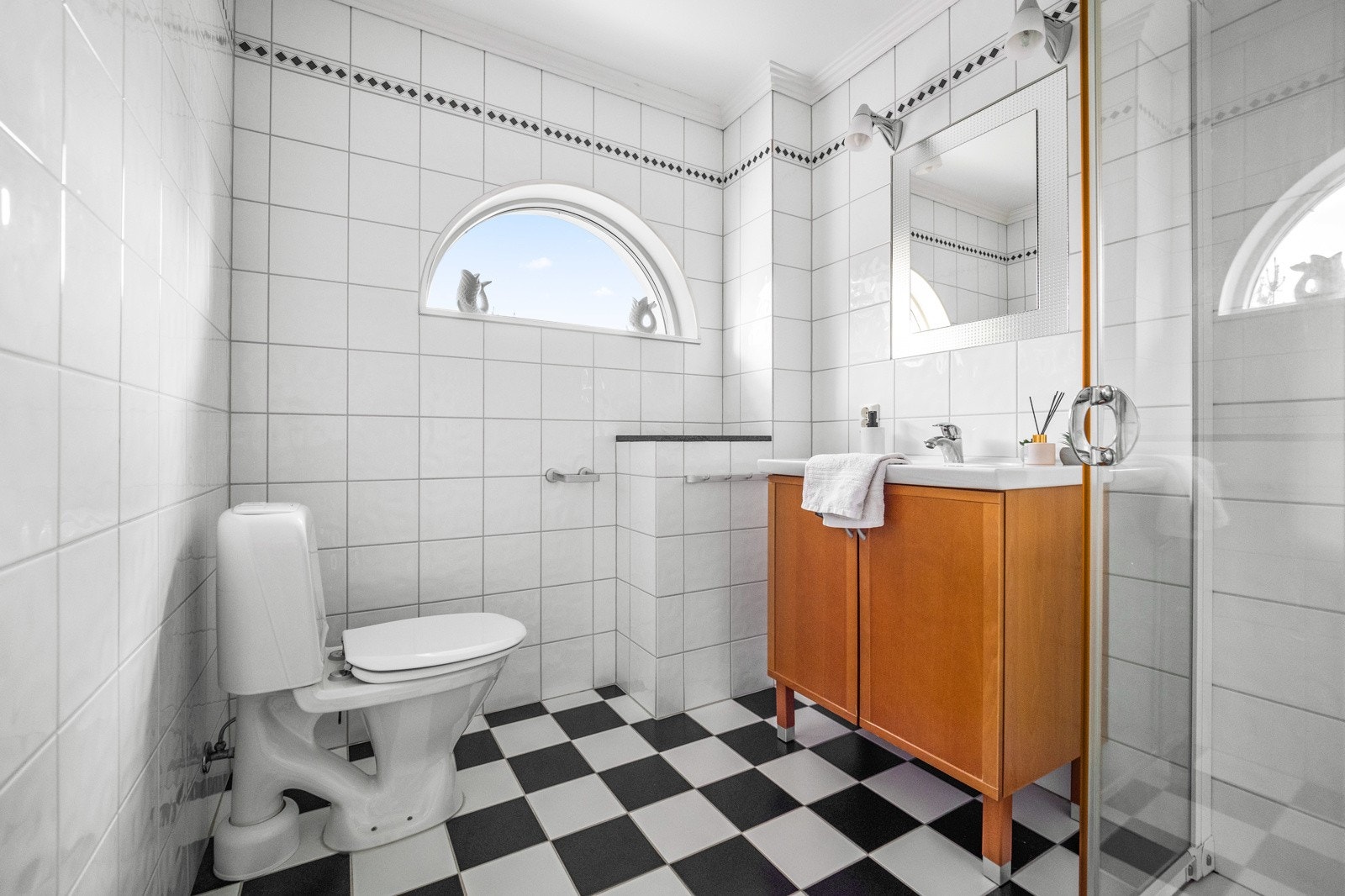 Det andre badet består av dusjhjørne med glassvegger, gulvmontert toalett og servant med tilhørende innredning og speil. Også her er det flislagt gulv med varmekabler, flislagte vegger og malt himling Galleribilde