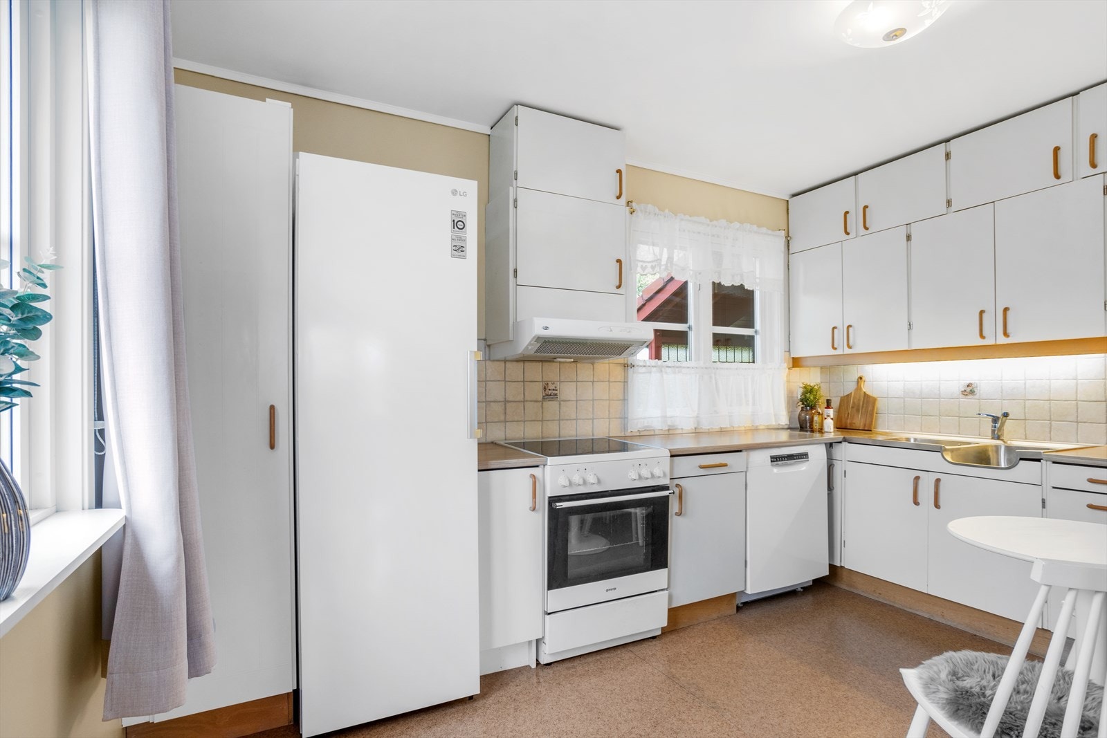 Hvit, eldre kjøkkeninnredning med slette fronter. Avsatt plass til kjøleskap, komfyr og oppvaskmaskin. Kjøkkenet er godt utstyrt med skapplass. Galleribilde