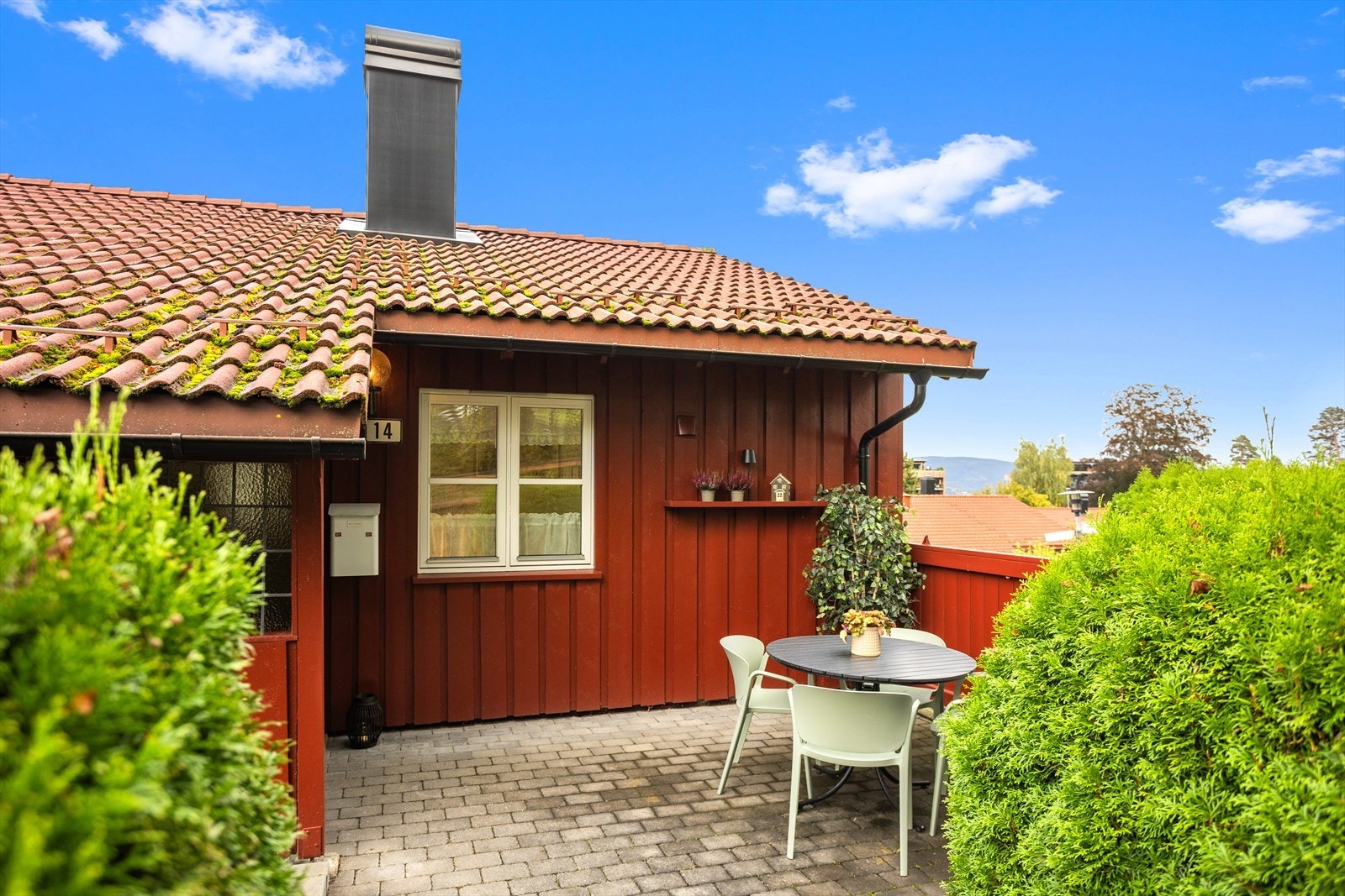 Inngangspartiet er lagt med belegningsstein og omkranset av frodig beplantning og skjermende busker. Galleribilde