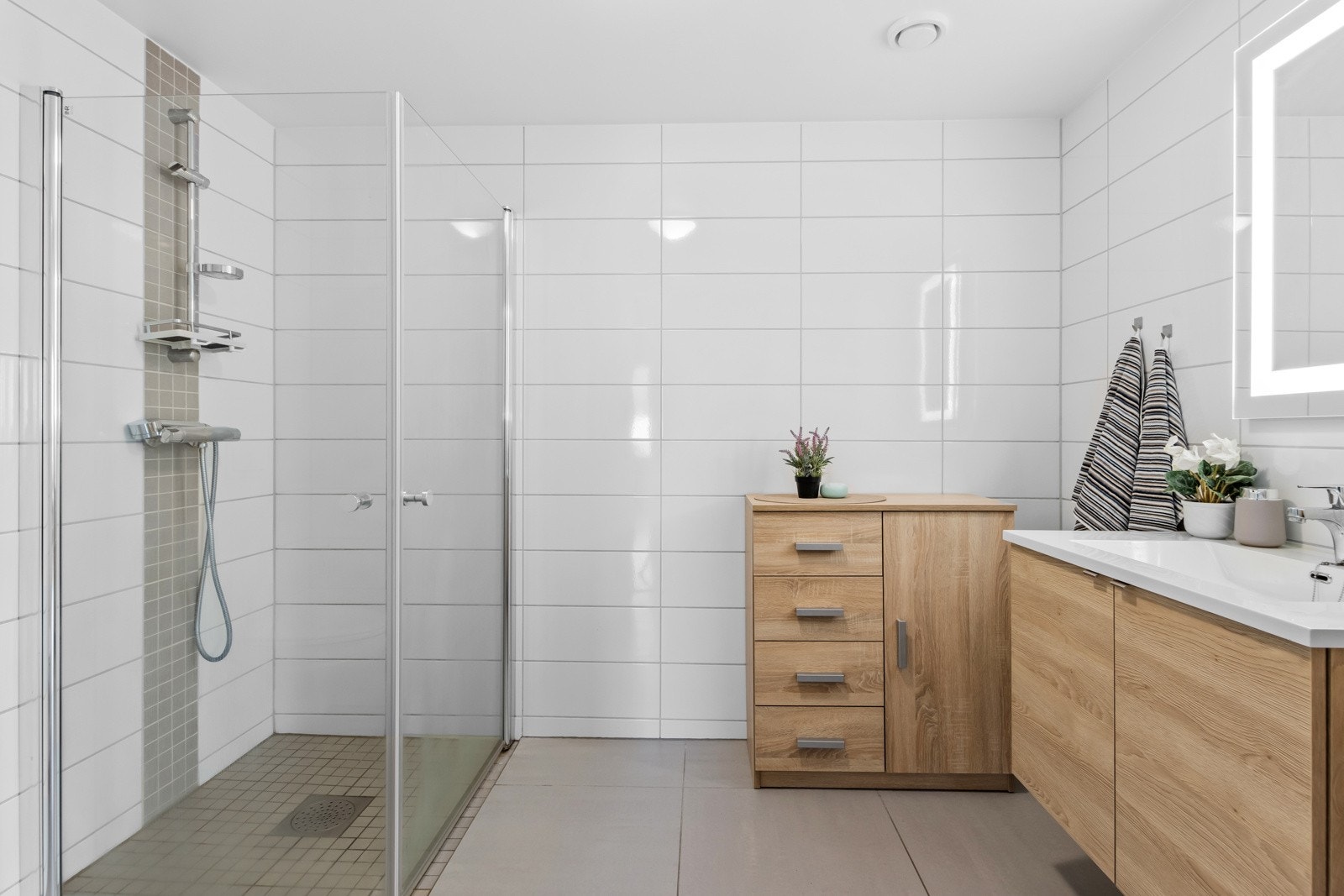 Delikat, flislagt bad med dusj, servant med skuffer, høyskap og vegghengt toalett. Galleribilde