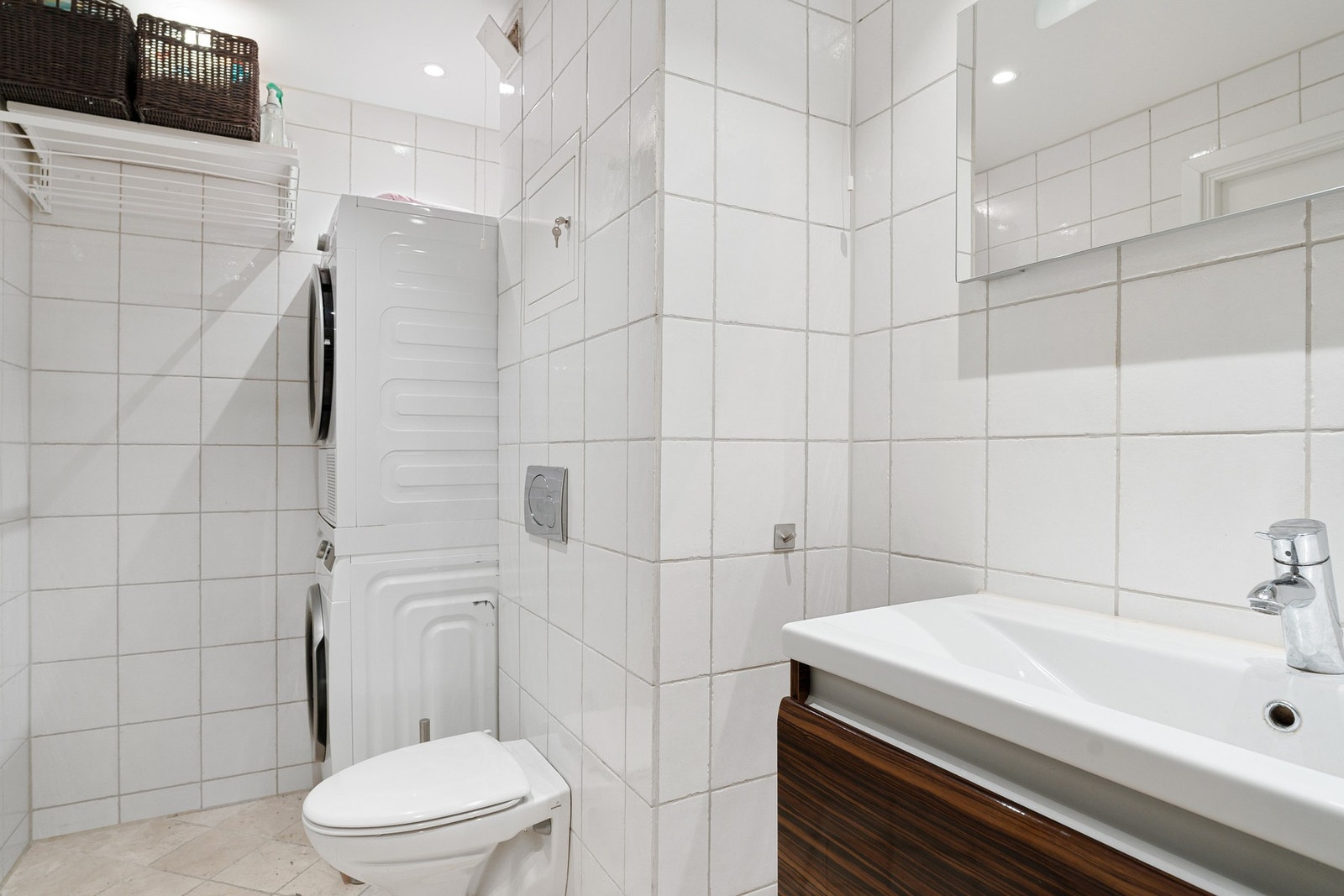 Badet er innredet med vegghengt servantinnredning, vegghengt speil med innebygd lys, dusjhjørne med buet innfellbare glassdører og vegghengt toalett med innebygget sisterne. Galleribilde