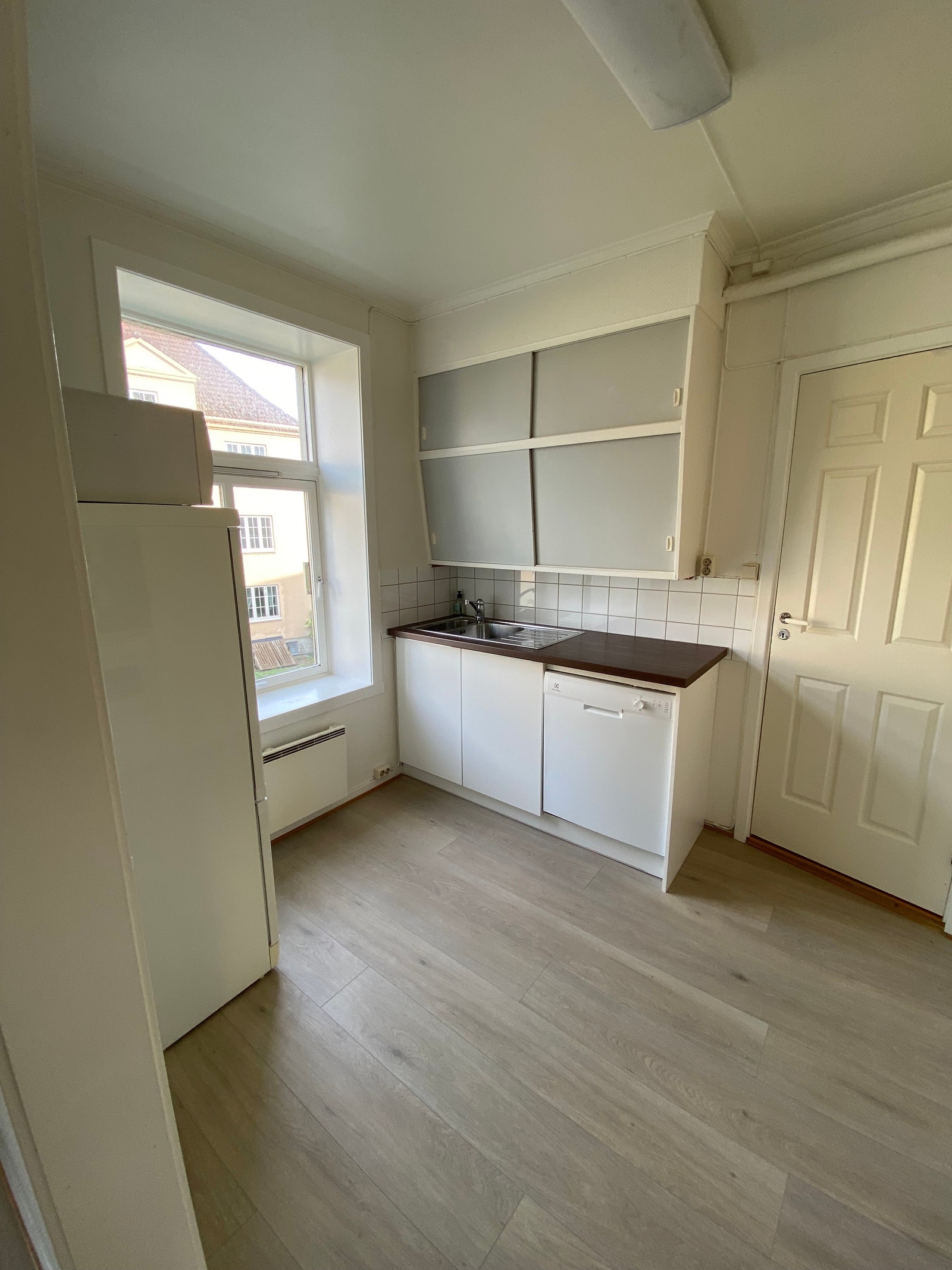 Kjøkken med godt lys fra stort vindu. Enstavs pergo på gulv, oppvaskmaskin, mikrobølgeovn, komfyr, kombiskap. Galleribilde