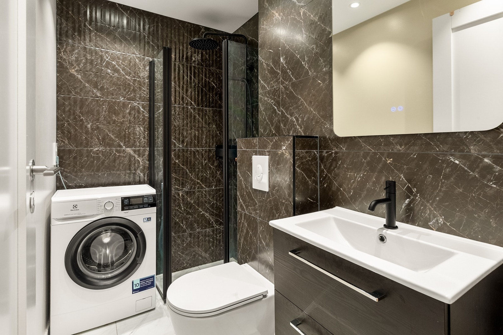 Et velutnyttet bad med en mørk, stilren innredning og opplegg for vaskemaskin. Galleribilde