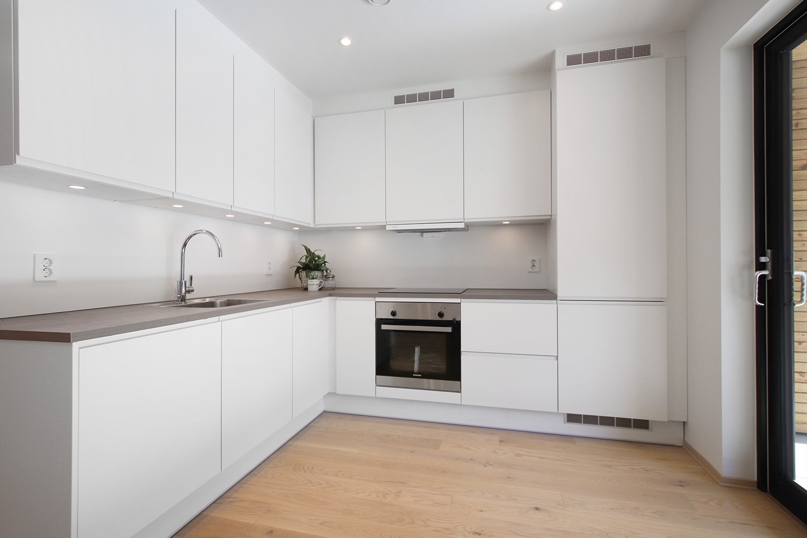 Lys kjøkkeninnredning med takhøye overskap og med integrerte hvitevarer. Galleribilde