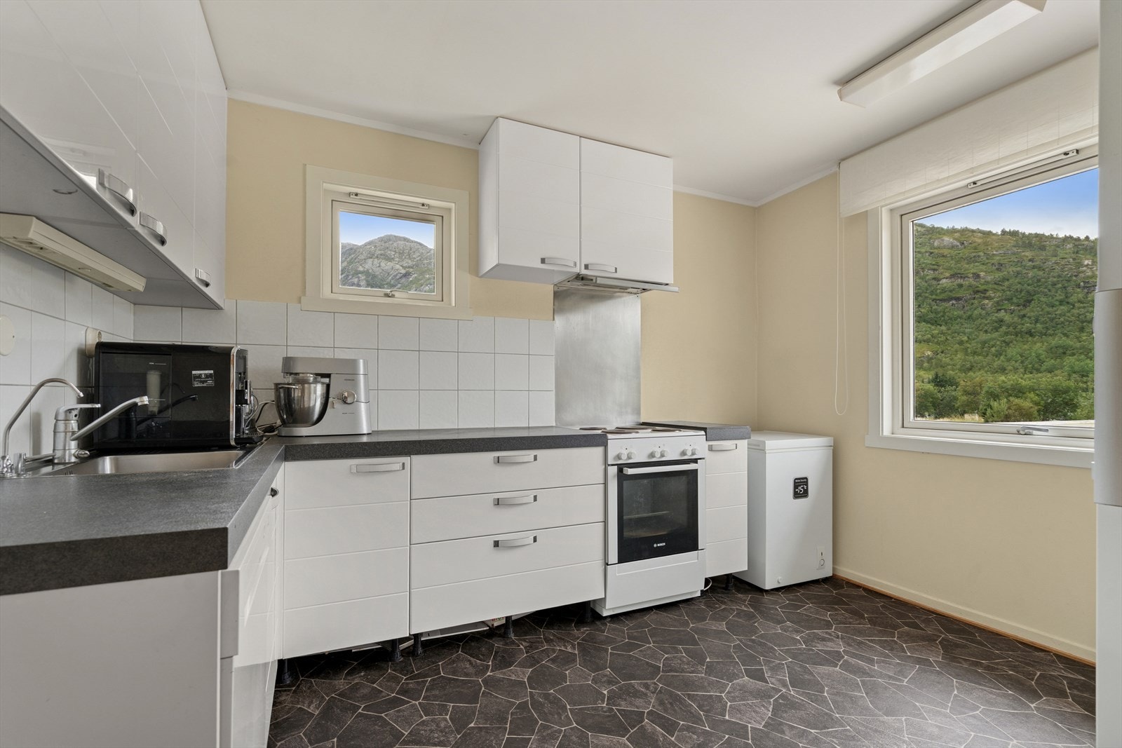 Innredet med glatte fronter, laminat benkeplate, kjøleskap, oppvaskmaskin og komfyr med avtrekk ut. Galleribilde