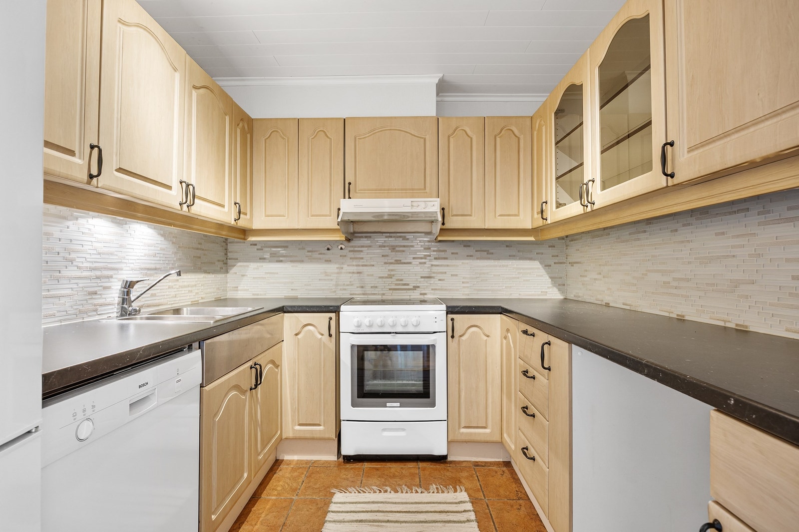 Boligens kjøkken har profilerte fronter og fliser på veggen over benkeplaten. Galleribilde